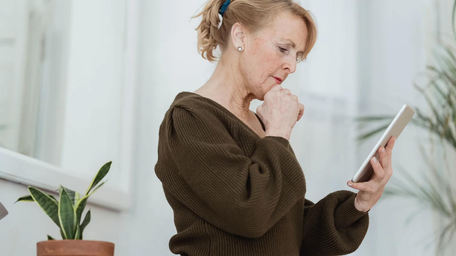 Une femme senior observe avec inquiétude l’écran de son smartphone à son domicile