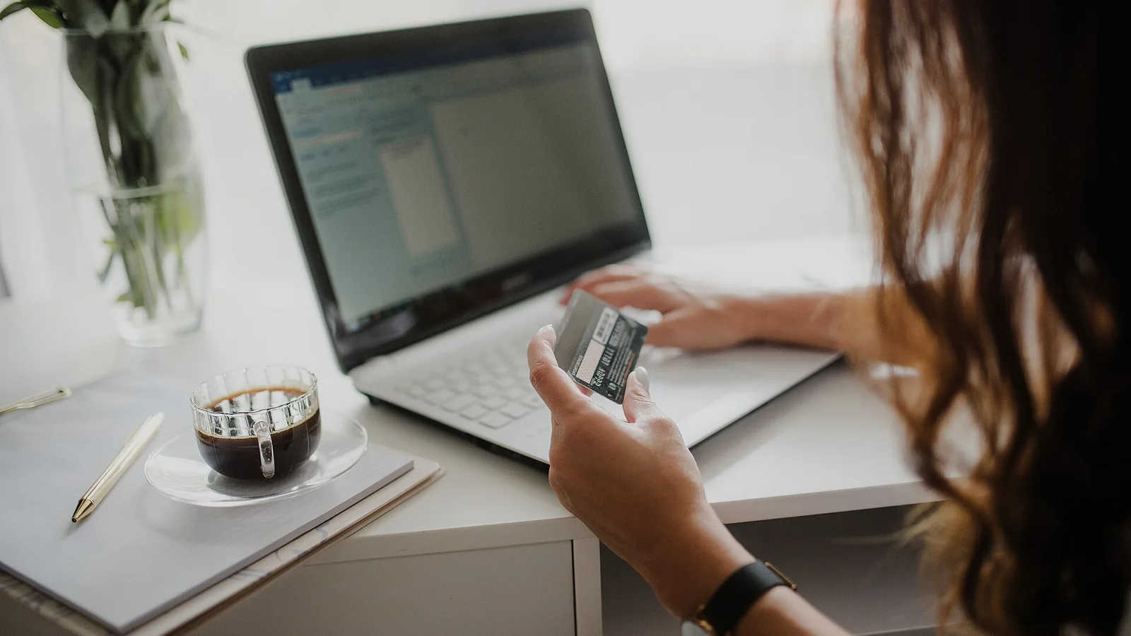 Une femme tient une carte bancaire devant son ordinateur portable lors d’un paiement en ligne