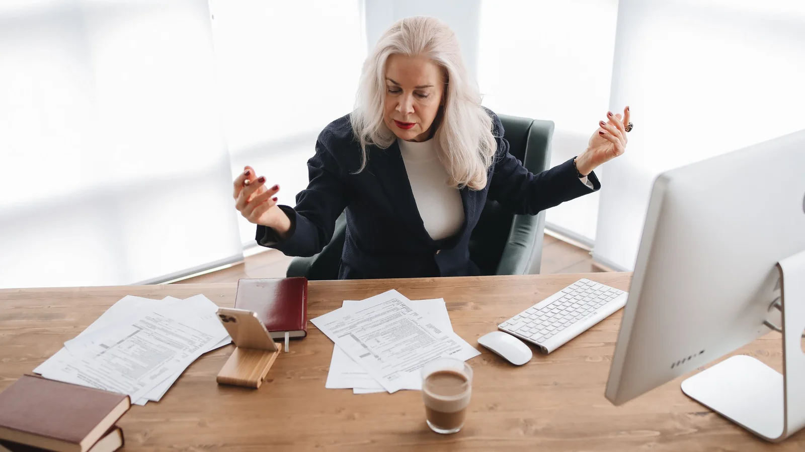 Une femme âgée assise à un bureau devant des documents administratifs et un ordinateur