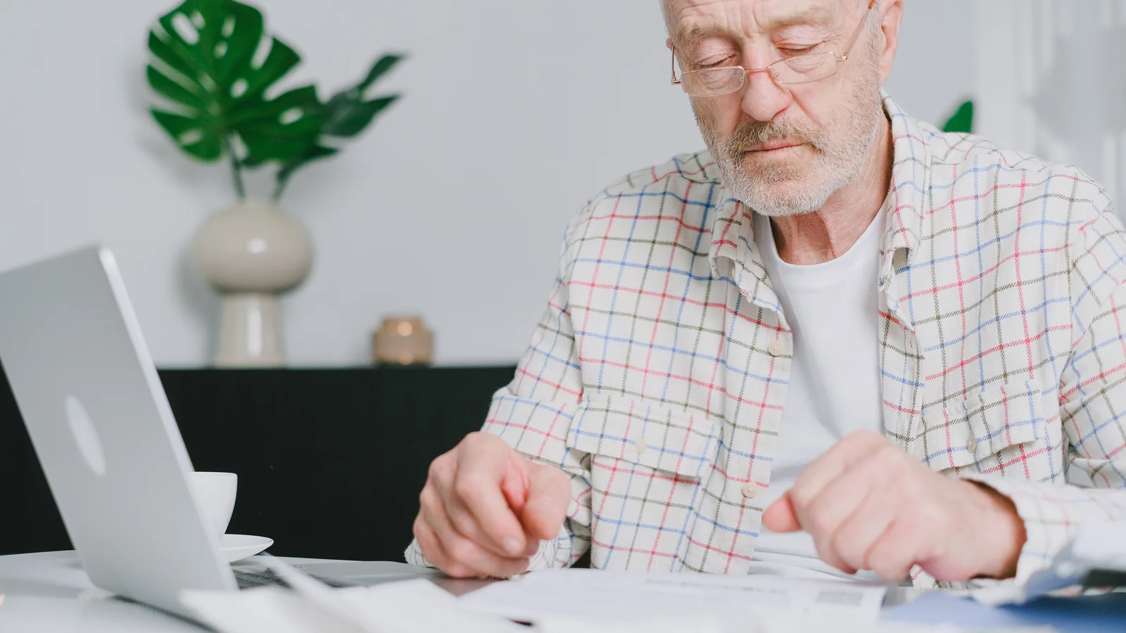 Un senior examine des documents financiers devant un ordinateur portable