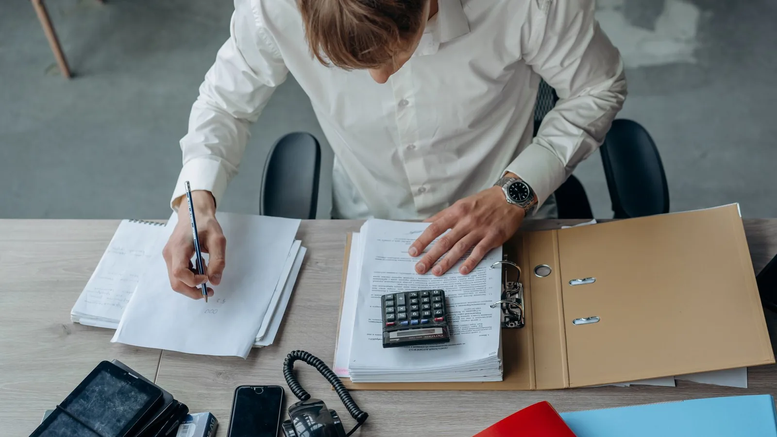 Un homme étudie des documents financiers avec une calculatrice à son bureau