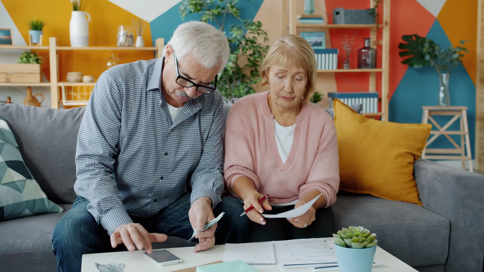 Un couple de seniors examine ses documents financiers et compte des billets dans son salon