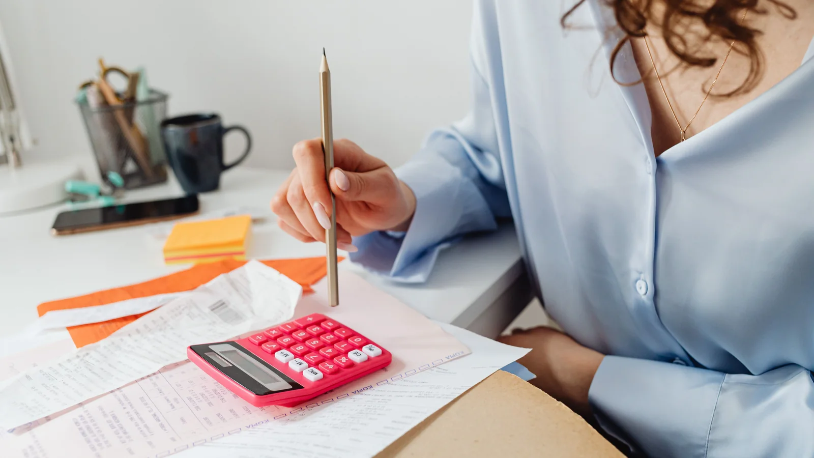 Une personne calcule ses dépenses avec une calculatrice et des relevés sur un bureau