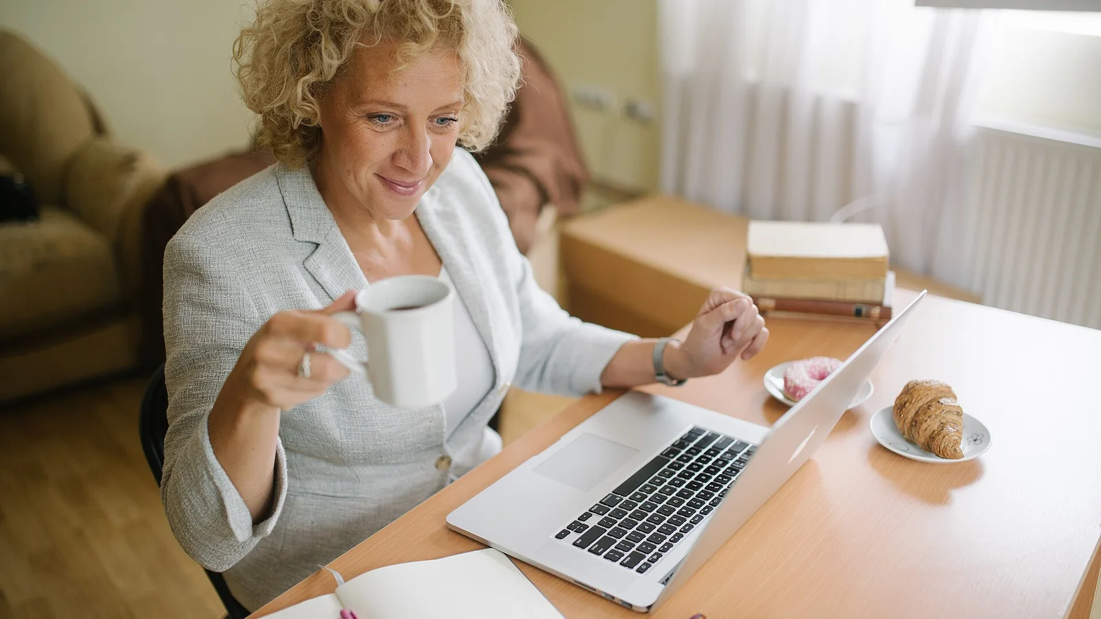 Une femme proche de la retraite consulte son ordinateur portable avec un carnet ouvert devant elle