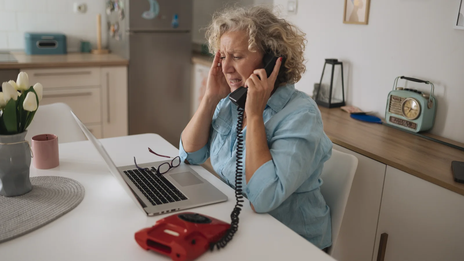 Une femme âgée téléphone devant un ordinateur portable pour effectuer une démarche bancaire