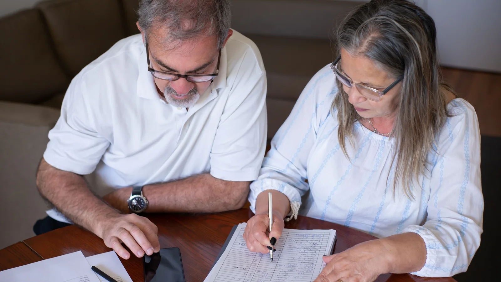 Un couple de retraités examine des documents financiers et un smartphone à son domicile