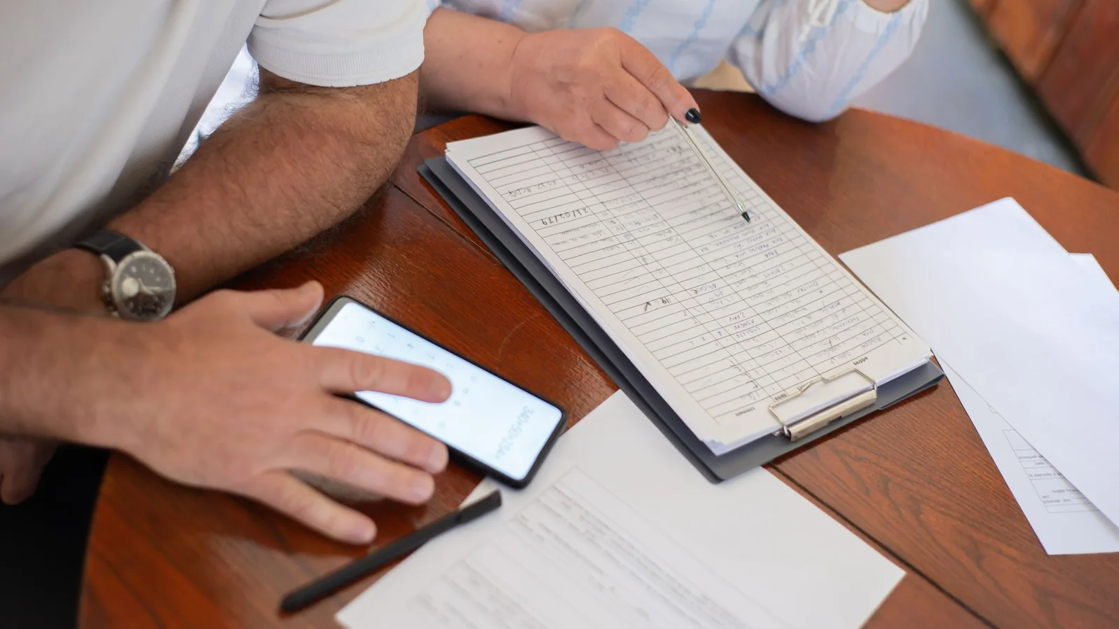 Les mains d’un couple de seniors examinant des documents et un téléphone sur une table