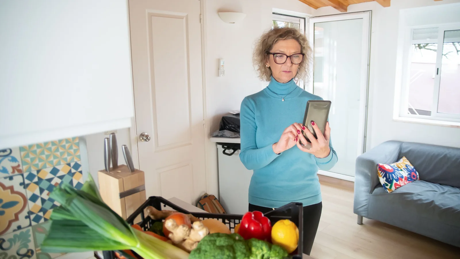 Une femme senior consulte avec attention son smartphone dans sa cuisine