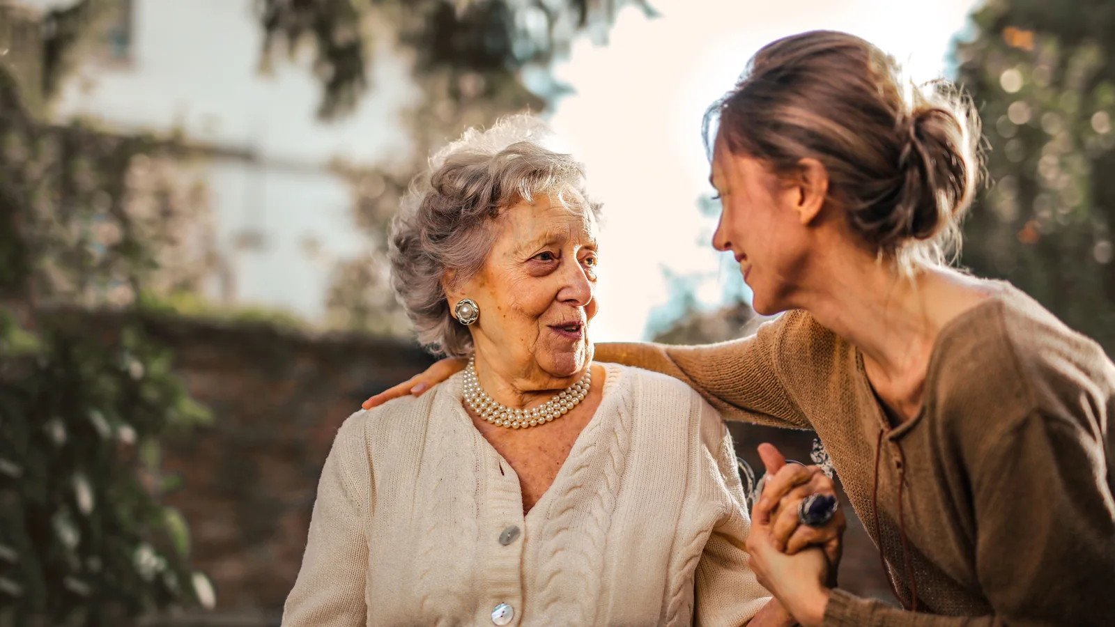 Une mère âgée et sa fille adulte s’embrassent dans un jardin, illustration d’une transmission familiale