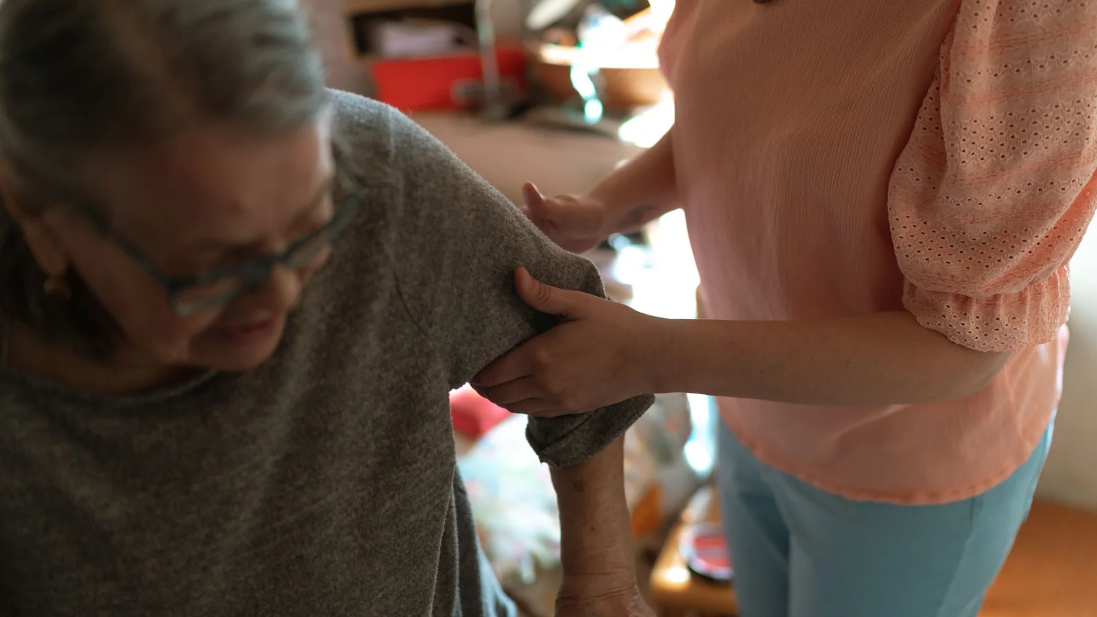 Une aidante soutient une femme âgée qui se déplace avec une canne à son domicile