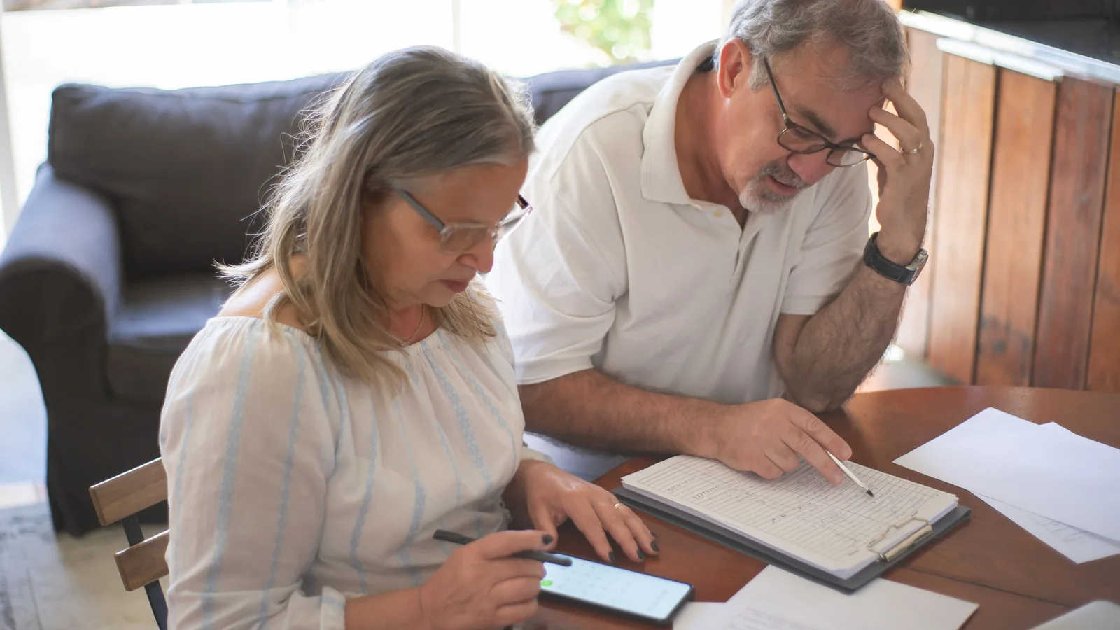 Un couple de seniors consulte des documents et un smartphone pour préparer la transmission de son patrimoine