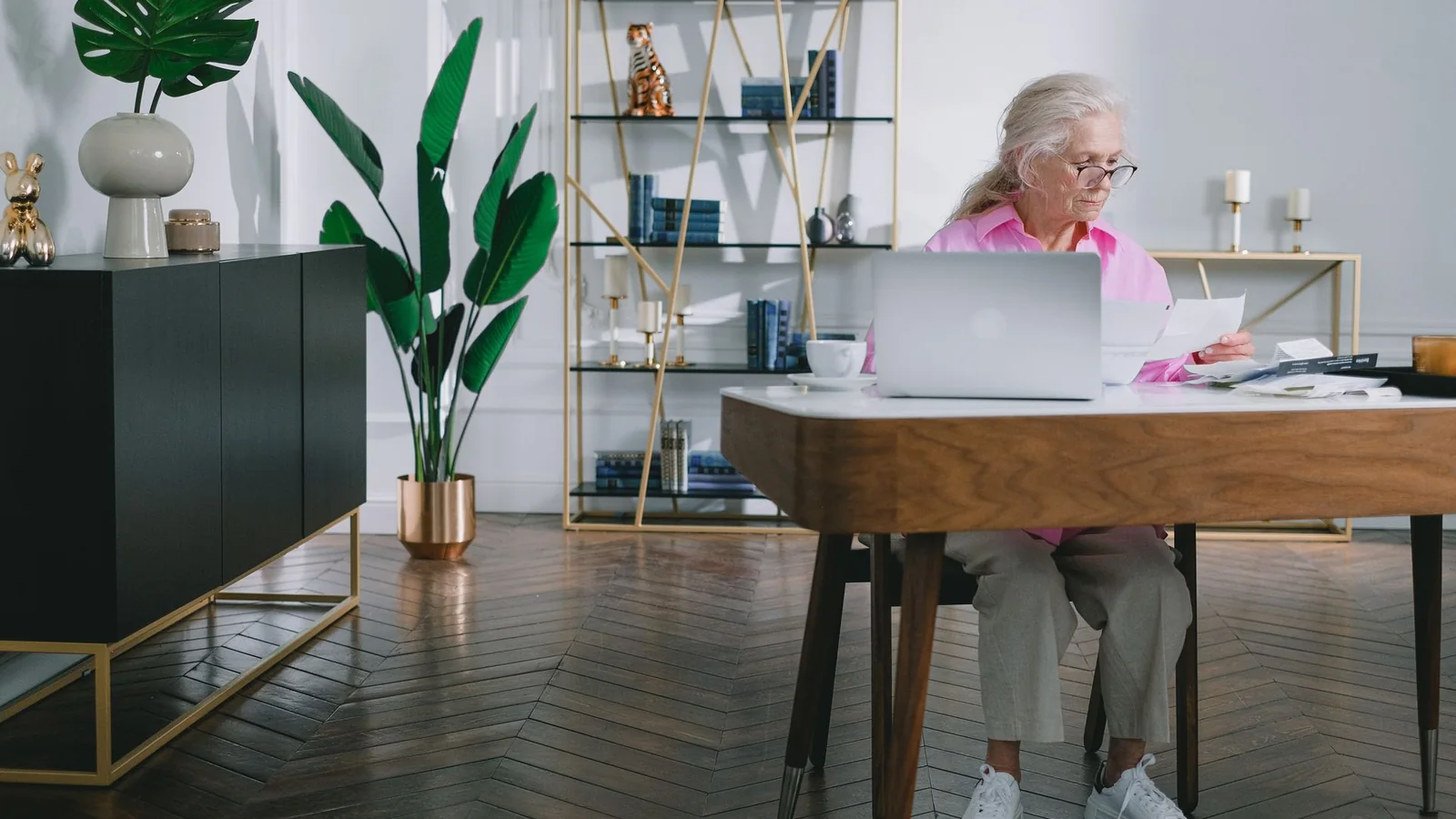 Une femme âgée examine des courriers et des documents devant son ordinateur portable