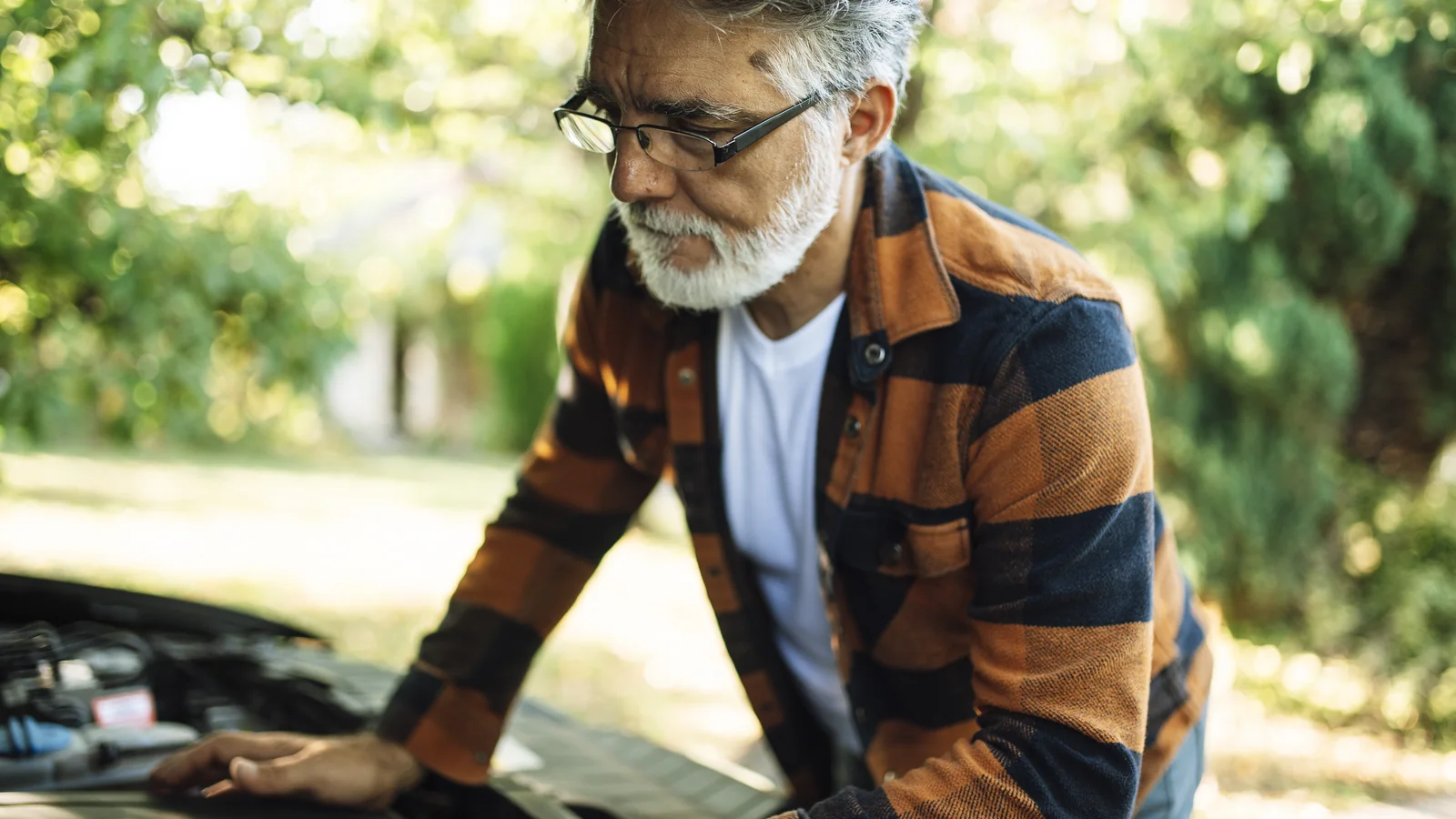 Un travailleur senior examine le moteur d’une voiture, une scène illustrant l’emploi des seniors