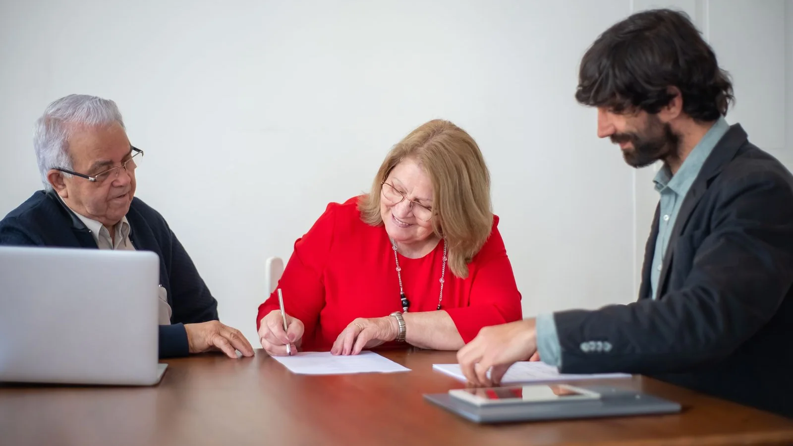 Une salariée senior signe un document avec 2 interlocuteurs autour d’une table de bureau