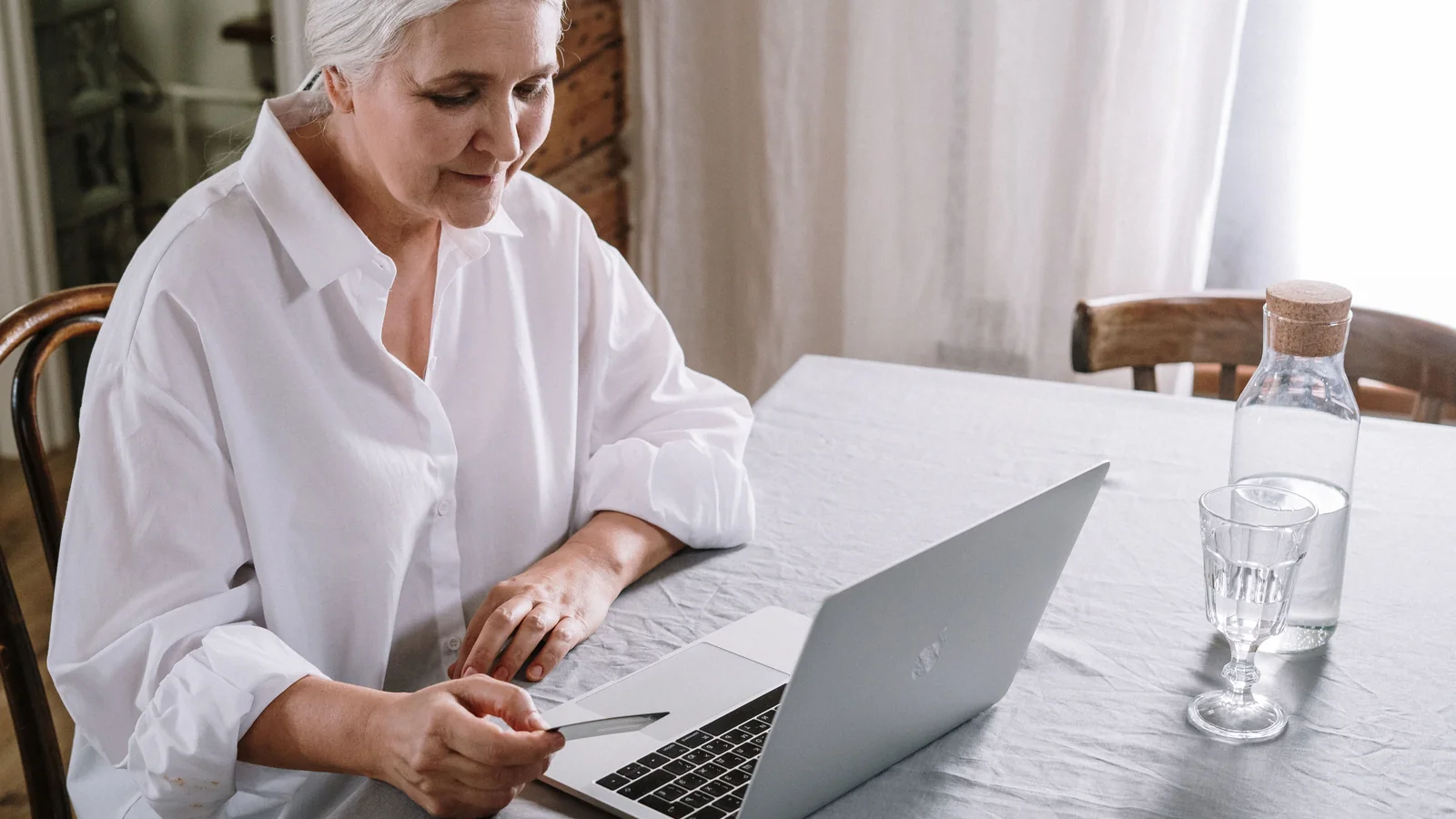 Une femme âgée consulte un ordinateur portable à son domicile, illustration des faux courriels visant les retraités