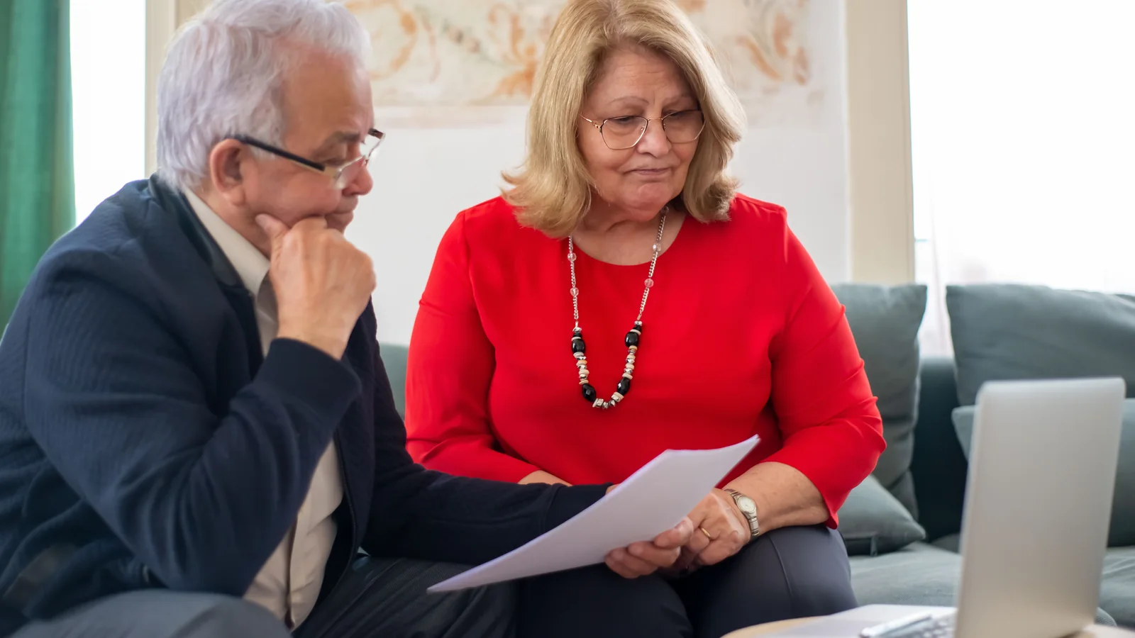 Un couple de retraités consulte des documents devant un ordinateur portable