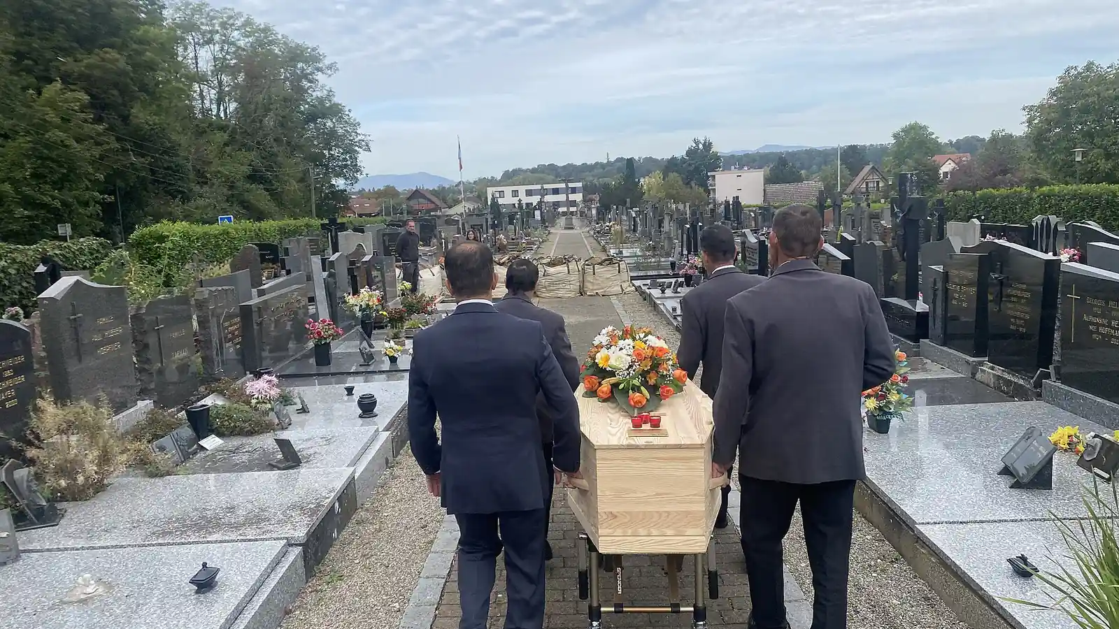 Des agents funéraires accompagnent un cercueil dans un cimetière en France