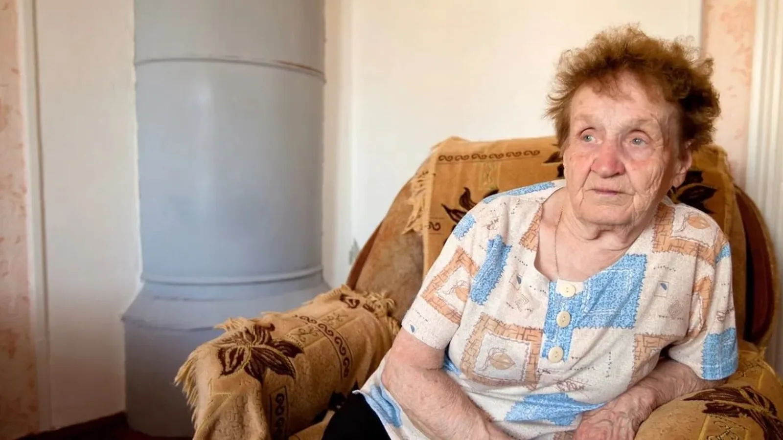 Une femme âgée assise dans son fauteuil à son domicile, illustrant les obstacles qui limitent les sorties