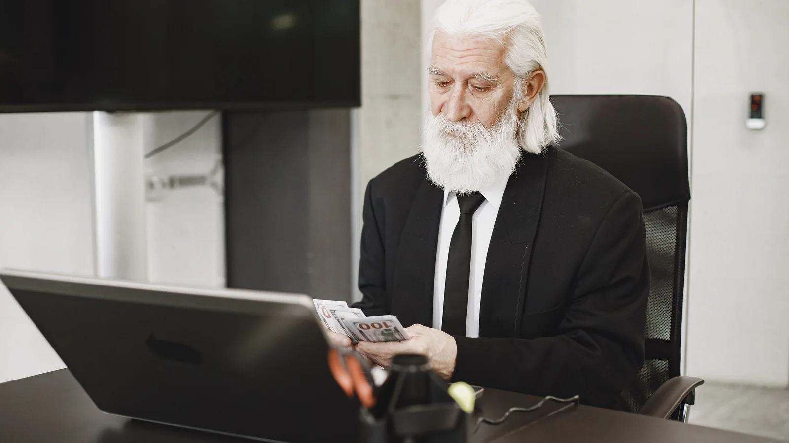 Un homme senior compte des billets devant son ordinateur portable dans un bureau