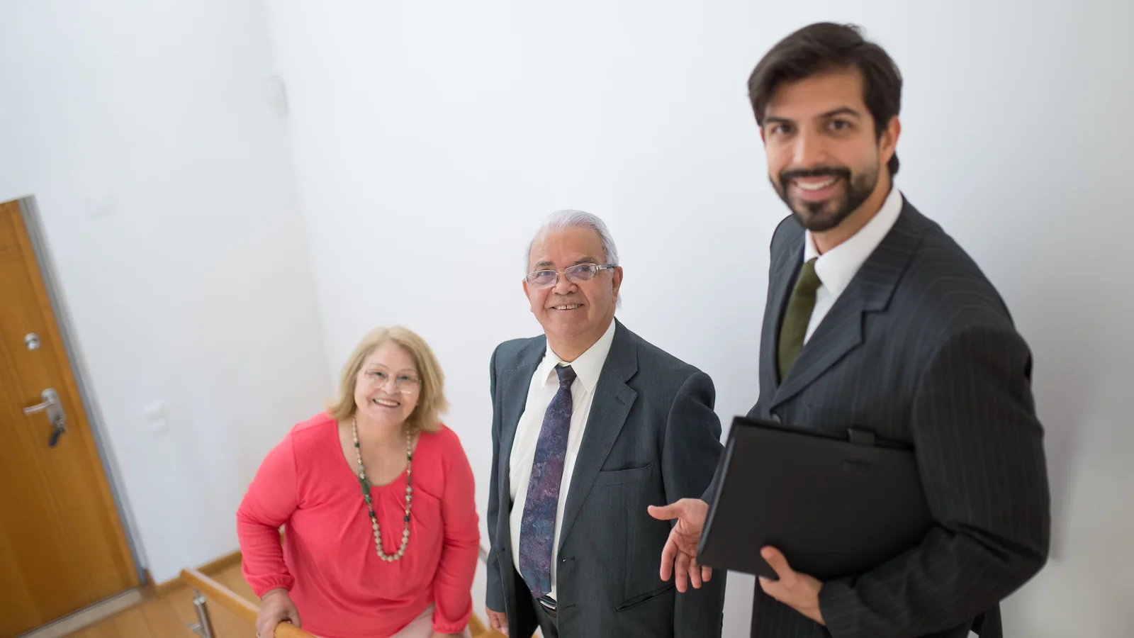 Un couple âgé accompagné par un agent immobilier dans l'escalier d'un logement