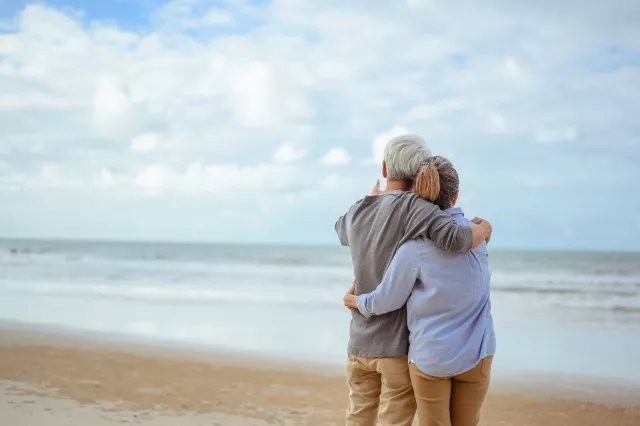 A senior couple hugged each other at the beach in the morning. The old man pointed the finger to the old woman to look at the bright blue sky, life insurance plan at the retirement concept.