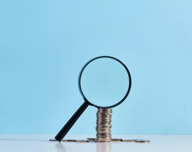 A stack of metal coins and a plastic magnifier on a blue backgro