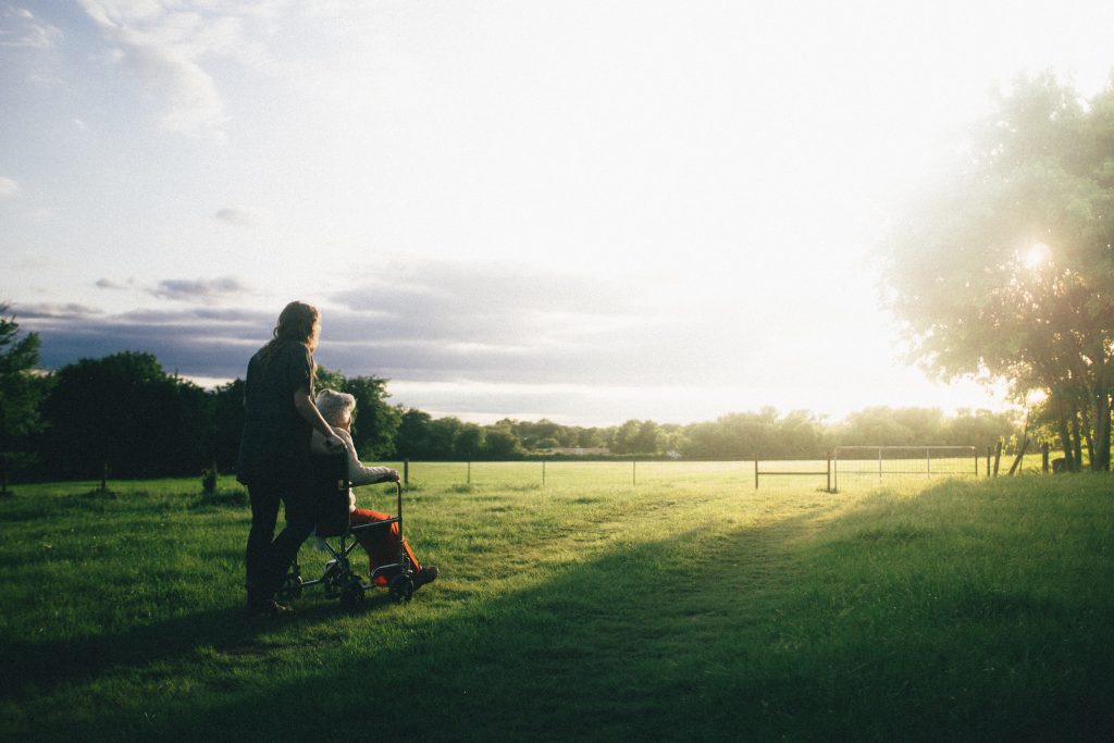 Dame qui pousse une personne âgée en fauteuil roulant sur l'herbe